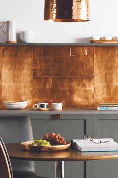 a wooden table topped with a plate of fruit next to a metal light hanging from the ceiling