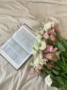 an open book and flowers on a bed with white sheets, pink and white tulips