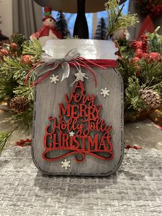 a mason jar with a merry message on it and christmas decorations in the back ground