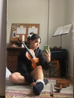 a woman sitting on the floor holding a violin in her hand and looking at her cell phone