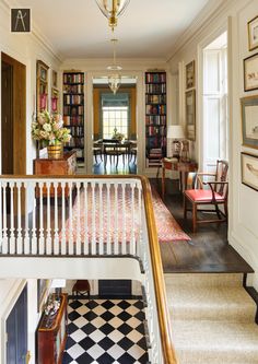 a staircase leading to a living room with bookshelves on the walls and a checkered floor