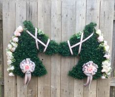 two wreaths made to look like animals with flowers and bows on them, sitting against a wooden fence