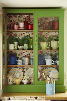 a green china cabinet filled with dishes and cups