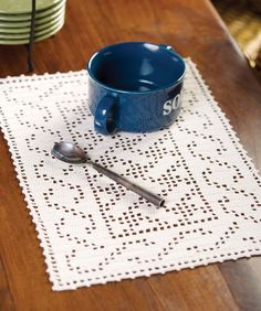 a blue cup and spoon sitting on top of a white placemat with doily