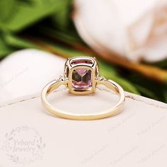 a pink tourmaline stone ring sitting on top of a white box with flowers in the background