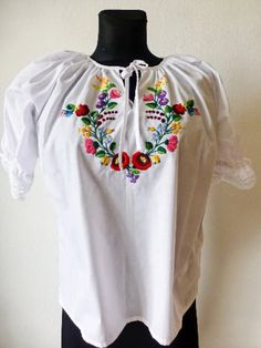 "This Hungarian traditional Kalocsa peasant blouse is the perfect addition to any boho or ethnic-themed wardrobe. With a beautiful floral pattern and intricate embroidery accents, this blouse will make you stand out in any crowd. Made from 100% cotton, this blouse has short sleeves and a collarless design, making it both comfortable and stylish. The blouse comes in XL size, perfect for a regular fit. This blouse is a great basic piece that can be dressed up or down for any occasion. Condition:new Size: L Bust 120cm(2 pieces) /47\" XL Bust 124cm/ 48.8\" International sizes:        XSS        M         LXL                 34 36/38 38/40 42 44  More from my shop: https://theoldworldvintage.etsy.com/listing/1561370024 Please,check my home decor shops : https://www.etsy.com/shop/HajniVintage Ka Spring Bohemian Blouse With Motif, Bohemian Spring Blouse With Motif, White Folk Peasant Top For Festival, Bohemian Blouse With Motif For Spring, Folk Style Embroidered Peasant Top For Festivals, Folk Style Peasant Top With Multicolor Embroidery For Festival, Folk Peasant Top With Multicolor Embroidered Neckline, Folk Blouse With Multicolor Embroidery Motif, Folk Style Multicolor Embroidered Peasant Top For Festivals