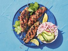 two skewered meats with cucumbers and onions on a blue plate