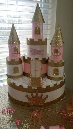 a pink and gold princess castle cake sitting on top of a table next to a window