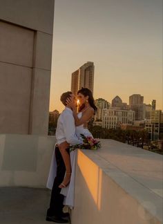 a bride and groom kissing on the roof of a building with city lights in the background