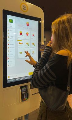 a woman standing in front of a vending machine and pointing to the menu on it