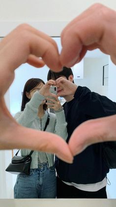 two people holding their hands in the shape of a heart with one person taking a photo