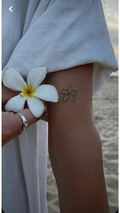 a person with a flower tattoo on their arm next to the ocean and sand at sunset