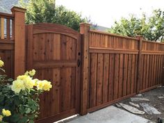 a wooden fence with yellow flowers in the foreground and a brick walkway leading up to it