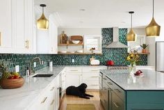 a black dog laying on the floor in a kitchen with white cabinets and green backsplash