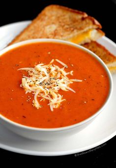 a white plate topped with a bowl of tomato soup next to a grilled cheese sandwich