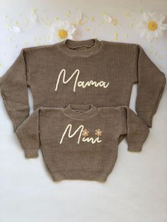 two sweaters with the words mama and baby written on them, sitting next to flowers