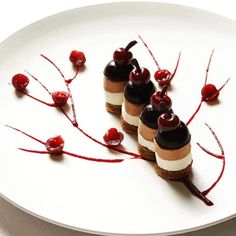 three small desserts on a white plate with red sauce and cherries are garnished