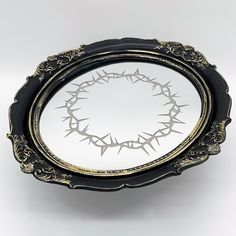 a black and gold plate with a crown of thorns design on the rim, against a white background