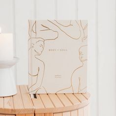 a book sitting on top of a wooden table next to a white vase and candle