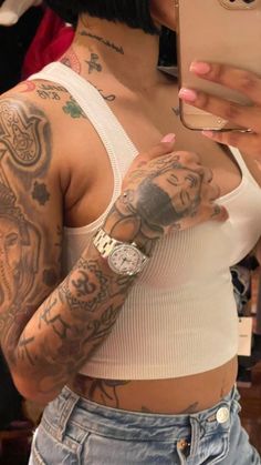 a woman with tattoos on her arm holding a cell phone and taking a selfie