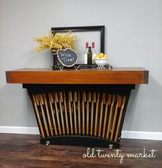 a wooden table with wine bottles and other items on top of it in front of a gray wall