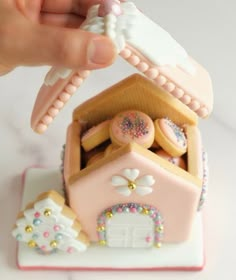 a hand is holding a miniature house made out of sugar and sprinkles