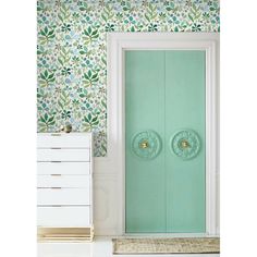 a green door is in front of a white dresser and wallpapered with flowers