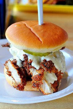 a chicken sandwich on a bun with pickles and mayonnaise sitting on a white plate