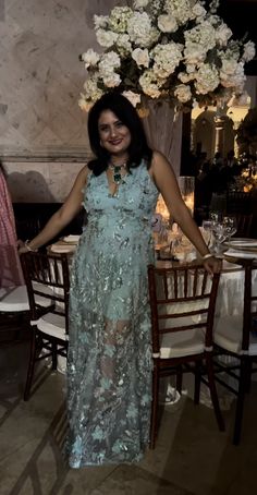 a woman standing in front of a table with flowers on it and wearing a blue dress