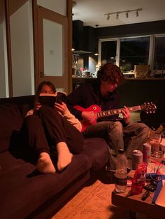 two people sitting on a couch playing guitars