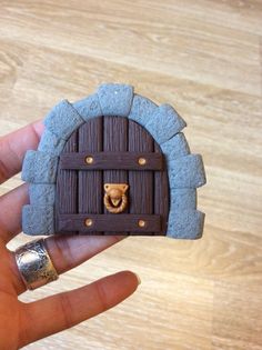 a hand is holding a miniature house made out of clay