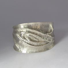 The ancient metal-sculpting method of chasing and repoussé was used to make artwork around the globe, from the mask of Tutankhamun to the Statue of Liberty. This argentium sterling silver cuff bracelet features a sinuous wave-like raised design, comfortable curved edges, and a contoured fit. Chasing and repoussé is a labor-intensive, high-contact process. First, I embed sheet metal in a cast-iron bowl filled with a mixture of pine pitch and brick dust. Using a chasing hammer and a series of specialized steel punches, I gradually push the metal into higher and higher relief, softening it between sessions with high heat as the hammering quickly makes the metal go hard and rigid. It took several days to make this cuff, with multiple sessions of careful sculpting in the pitch bowl followed by Metal Sheet Jewelry, Artistic Hammered Silver Jewelry, Artistic Silver Cuff Bracelet, Silver Hand Cast Metal Cuff Bracelet, Unique Sculpted Silver Jewelry, Silver Metal Cuff Bracelet Hand Cast, Silver Polished Cuff Bracelet For Ceremonial Use, Silver Cuff Bracelet With Polished Finish For Ceremonial Use, Artisan Silver Hand Forged Cuff Bracelet