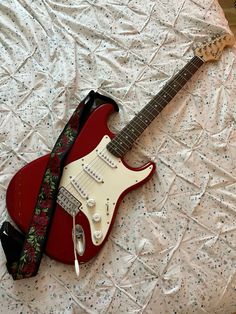 a red electric guitar laying on top of a bed next to a black and white strap