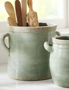 two green pots with spoons and spatulas in them sitting on a window sill