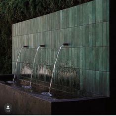 three water fountains in front of a green wall