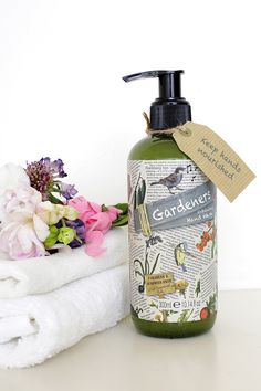 a bottle of soap sitting next to a pile of towels with flowers on it and a tag