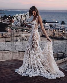 a woman standing on top of a wooden deck next to the ocean wearing a wedding dress