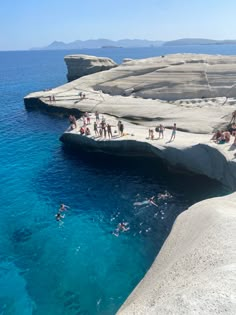 people are swimming in the blue water near cliffs