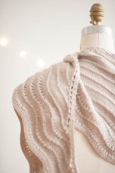 a white knitted shawl draped over a mannequin's dummy with lights in the background