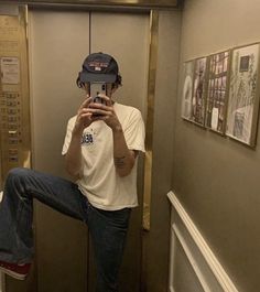 a man taking a selfie in the bathroom with his cell phone and hat on