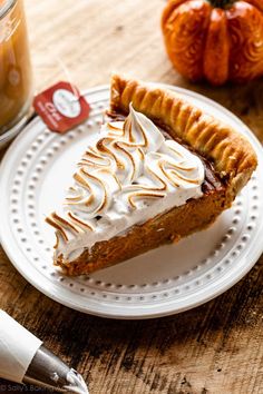 a piece of pie on a white plate next to a cup of coffee and an orange pumpkin