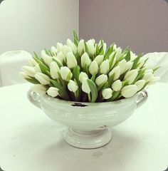 a white bowl filled with lots of flowers on top of a table