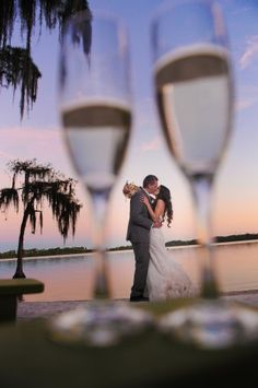 a bride and groom standing next to each other with wine glasses in front of them