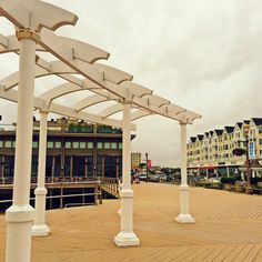 an empty boardwalk with white pillars and buildings in the backgroung, on a cloudy day