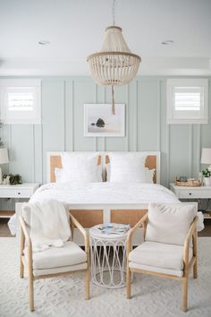 a white bed sitting next to two chairs and a table with a cat on it