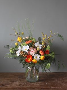 a glass vase filled with lots of flowers on top of a wooden table next to a gray wall