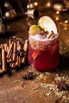 an apple and cinnamon drink in a glass surrounded by cinnamon sticks, cloves and star anise