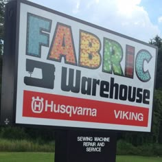 a large sign advertising fabric warehouse in front of some grass and trees with blue sky