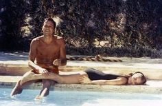 a man and woman are sitting in the water near a swimming pool, one is on her stomach