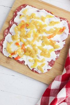 a wooden cutting board topped with food on top of a white table next to a red and white checkered towel